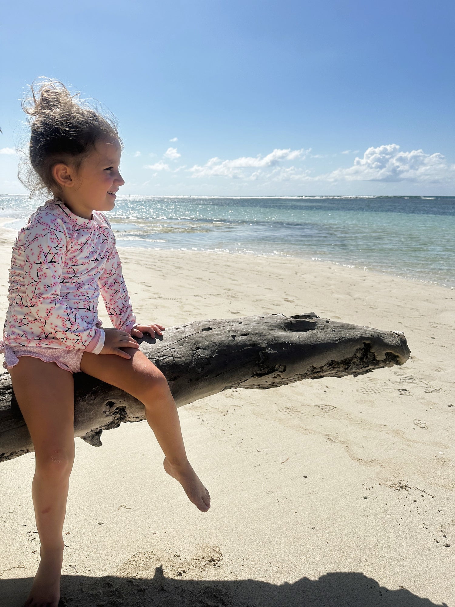 girl with long sleeve UV-protective shirt and swim trunks on a branch on the beach